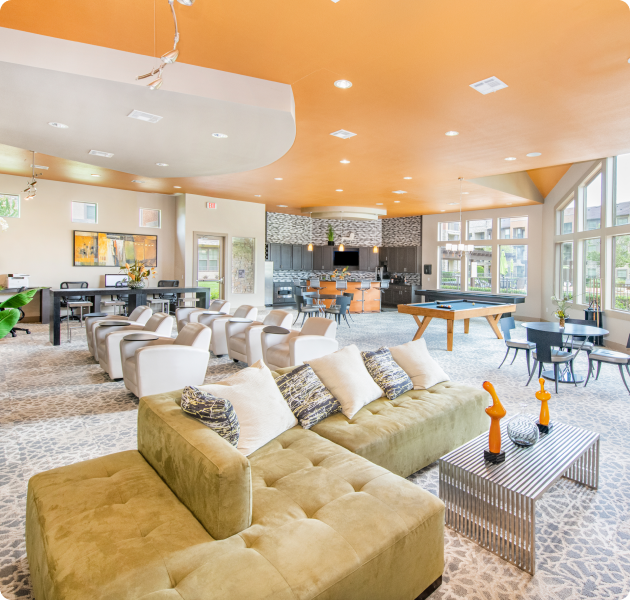 Modern community lounge area with orange accent ceiling, kitchen and coffee bar, a pool table and multiple seating areas on tile flooring next to the large picture windows at MAA Vintage Park luxury apartments in Houston, TX