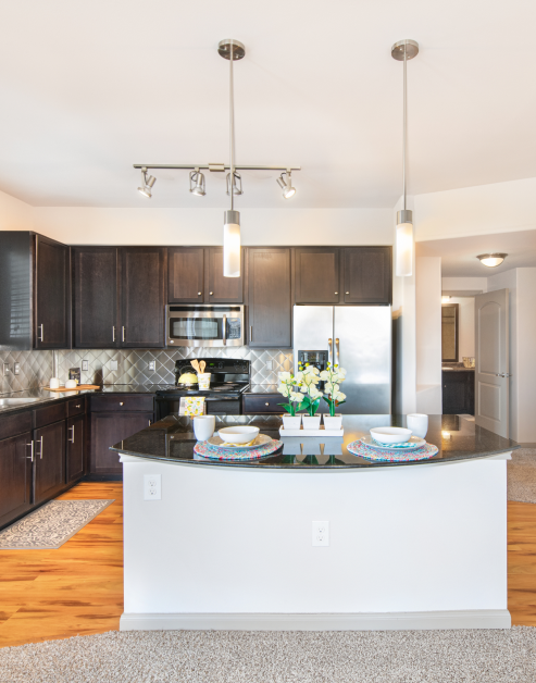 Modern kitchen with hanging light fixtures over a kitchen island and stainless-steel appliances with tile backsplash, dark brown cabinets and wood flooring at MAA Vintage Park luxury apartments in Houston, TX