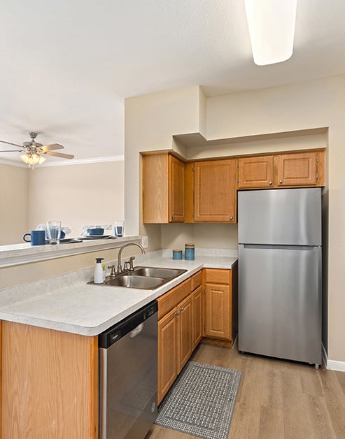Kitchen with double sink on white countertops with wooden cabinets, stainless steel appliances on wood floors at MAA Woodwind luxury apartments in Houston, TX
