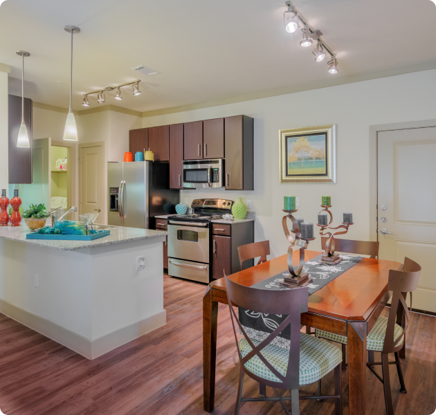 Open-style apartment kitchen with dark wood cabinets, white counters with stainless steel appliances on wood floors next to a dining area with a wooden dining table at MAA Bulverde luxury apartments in San Antonio, TX