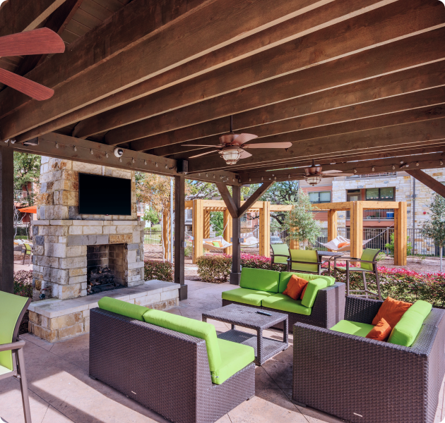 Community outdoor covered patio with ceiling fans, a brick fireplace with a wall-mounted TV and multiple seating areas at MAA Bulverde luxury apartments in San Antonio, TX
