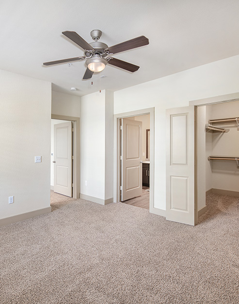 Empty master bedroom with a ceiling fan, carpeted floors, en-suite bathroom and walk-in closet at MAA Bulverde luxury apartments in San Antonio, TX