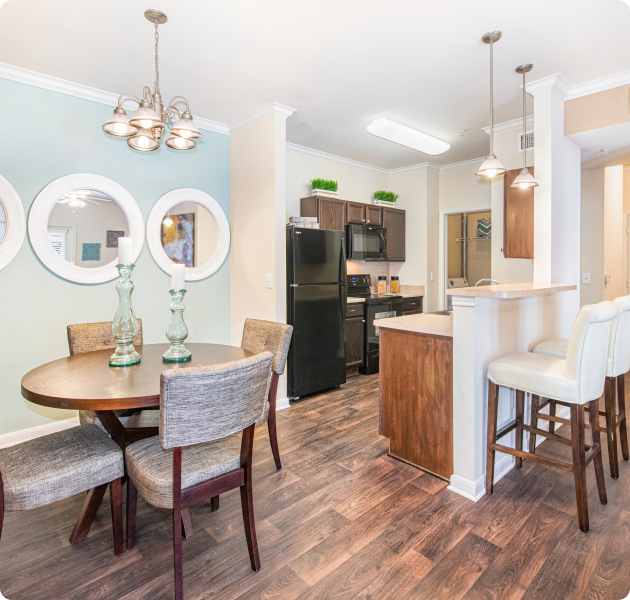 Apartment kitchen and dining area with a hanging light fixture above wood dining table and chairs next to an accent wall with round mirrors at MAA Haven at Blanco luxury apartments in the San Antonio, TX