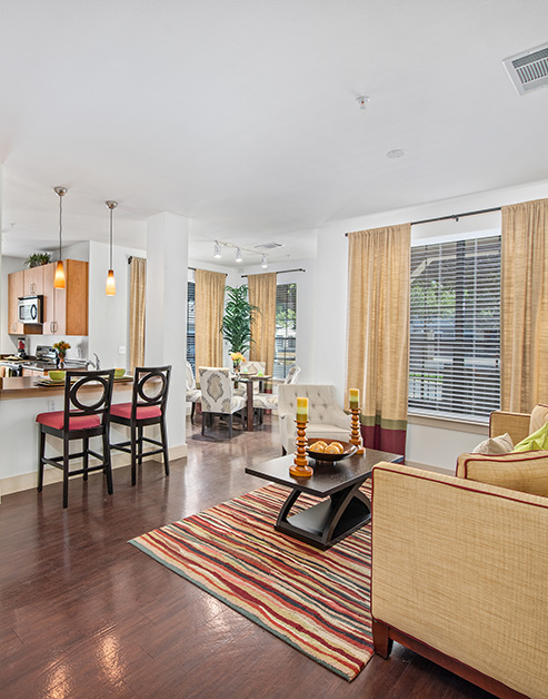 A spacious living room with a beige couch, armchair and wooden coffee table on wooden floor next to kitchen and dining area at MAA Westover Hills luxury apartments in San Antonio, TX