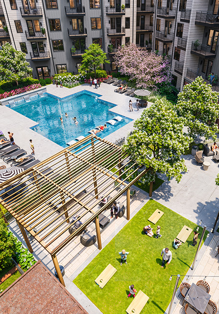 Aerial view of a landscaped apartment courtyard featuring a large swimming pool with lounge chairs next to a shaded seating area with a green lawn at MAA Rove luxury apartments in Richmond, VA