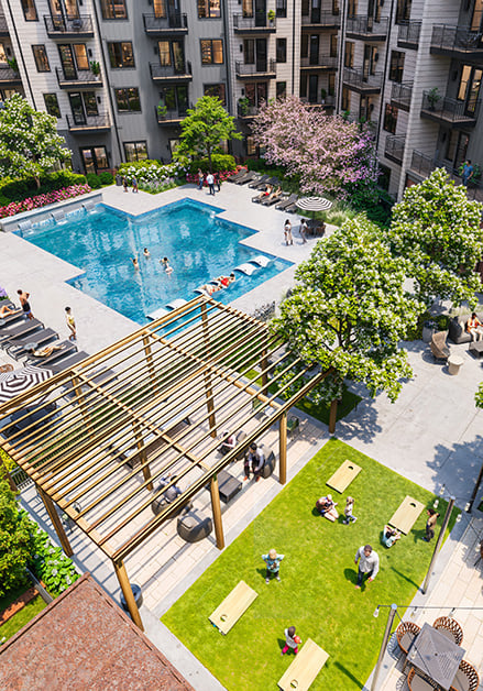Aerial view of a landscaped apartment courtyard featuring a large swimming pool with lounge chairs next to a shaded seating area with a green lawn at MAA Rove luxury apartments in Richmond, VA