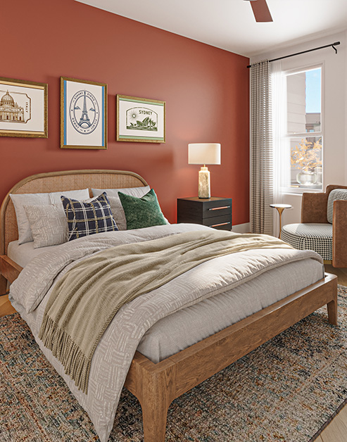Bedroom with a wooden bed next to a coral accent wall with framed artwork,  a large arched mirror, matching bedside nightstands on an area rug and wood floors at MAA Rove luxury apartments in Richmond, VA