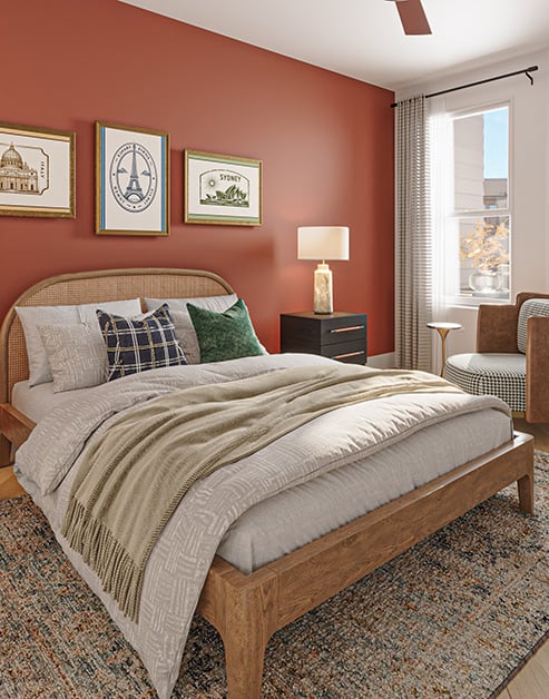 Bedroom with a wooden bed next to a coral accent wall with framed artwork, a large arched mirror, matching bedside nightstands on an area rug and wood floors at MAA Rove luxury apartments in Richmond, VA