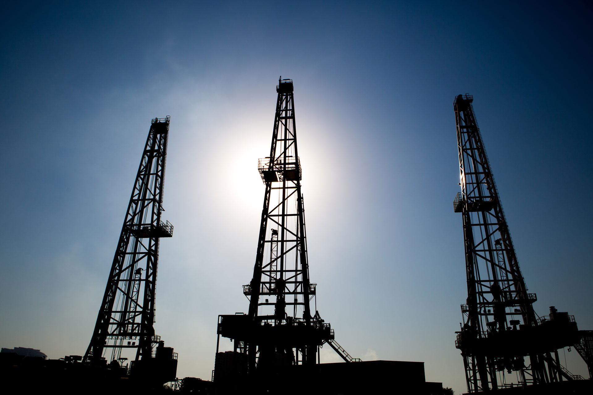 Upwards view of the tops of three oil rigs with a clear sky in the background