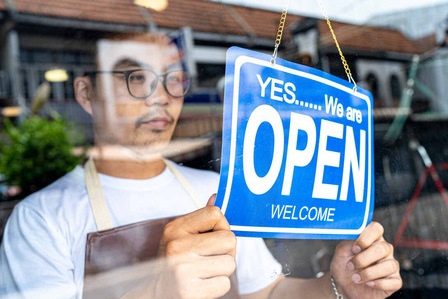 A man in a store window turning over the open sign to indicate that the store is open.