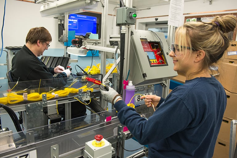 Workers assembling yellow cables on a production line inside an industrial manufacturing facility