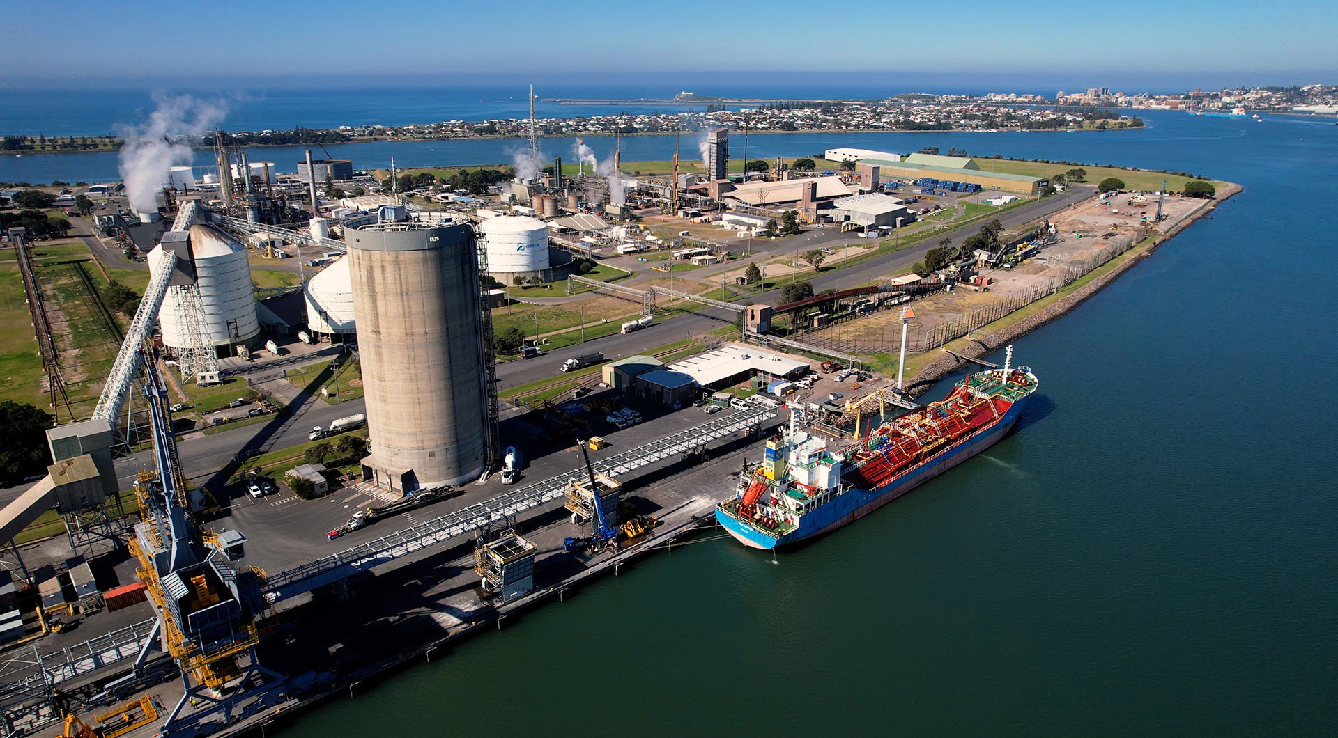 Aerial view of an industrial port facility with storage tanks, processing units, and a docked cargo vessel