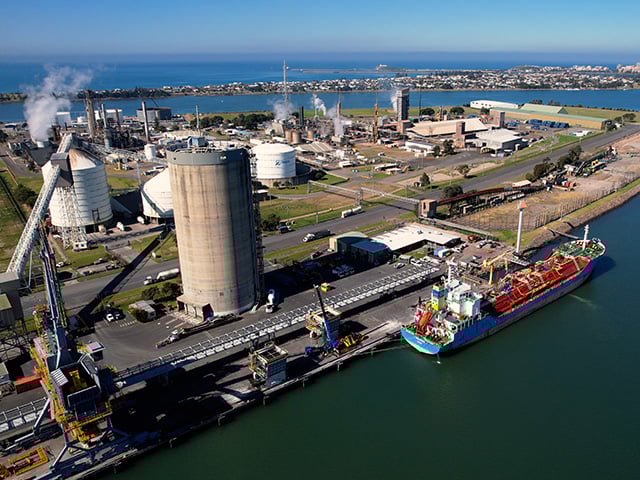 Aerial view of an industrial port facility with storage tanks, processing units, and a docked cargo vessel