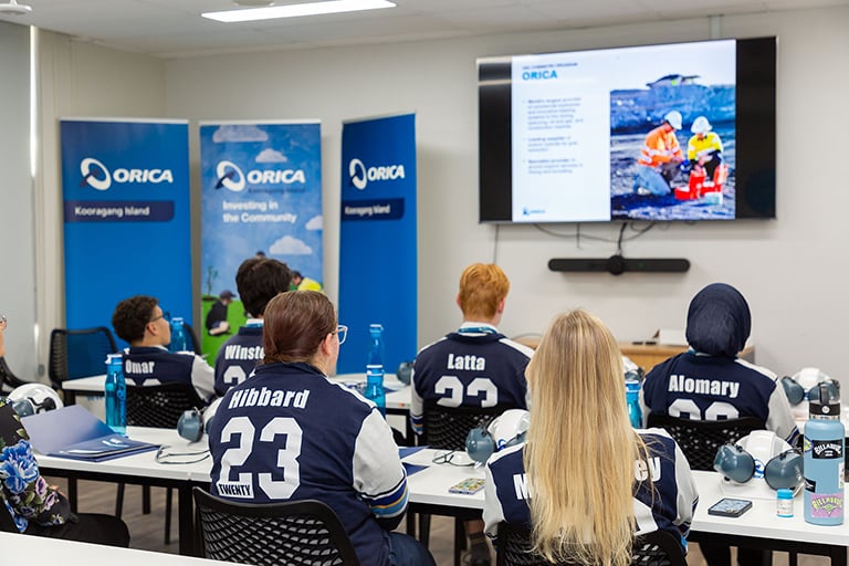 People attending a safety presentation in a training room with branded banners and a screen display