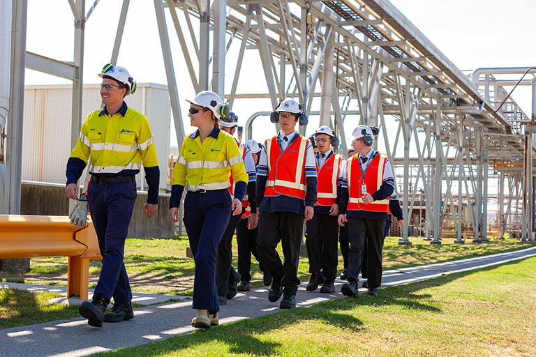 Group in high-visibility safety gear walking through an industrial plant with metal structures in the background