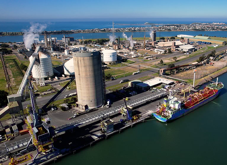 Aerial view of an industrial port facility with storage tanks, processing units, and a docked cargo vessel