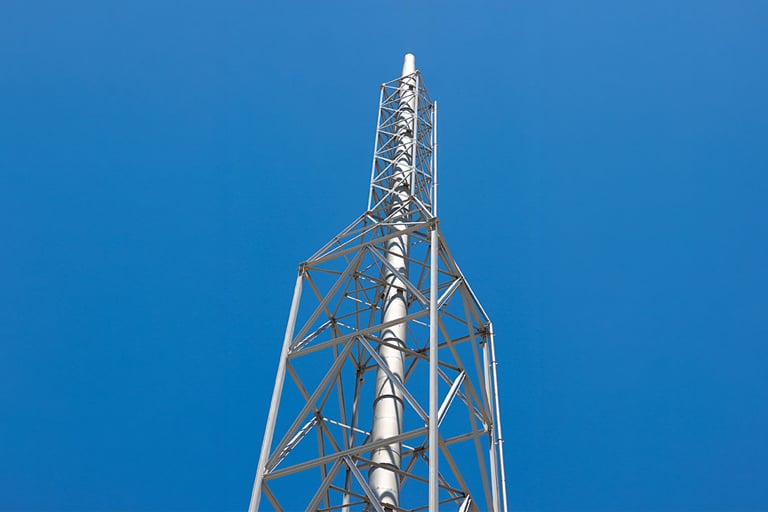 Tall industrial stack supported by a steel lattice against a clear blue sky