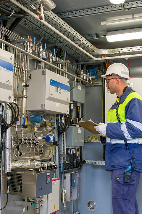 Worker in safety gear inspecting industrial control equipment inside a processing facility