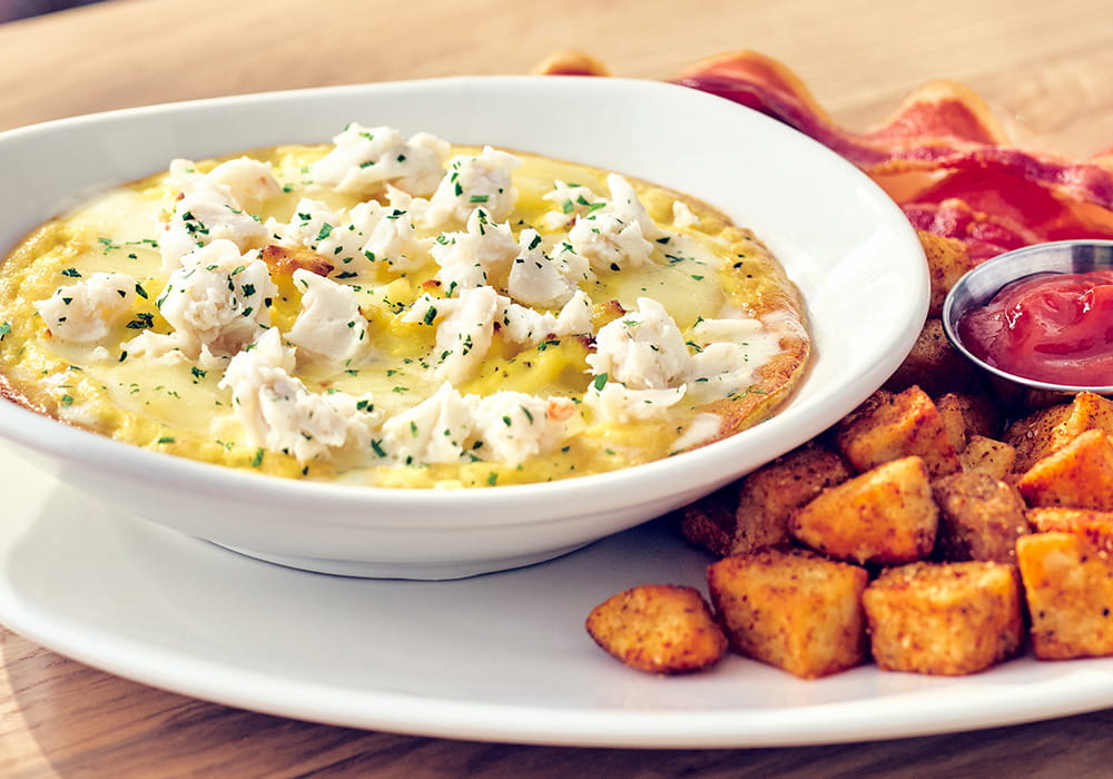 CRAB AND FONTINA CHEESE FRITTATA Egg soufflé topped with creamy Fontina cheese and lump crab meat, served with seasoned breakfast potatoes and applewood smoked bacon.