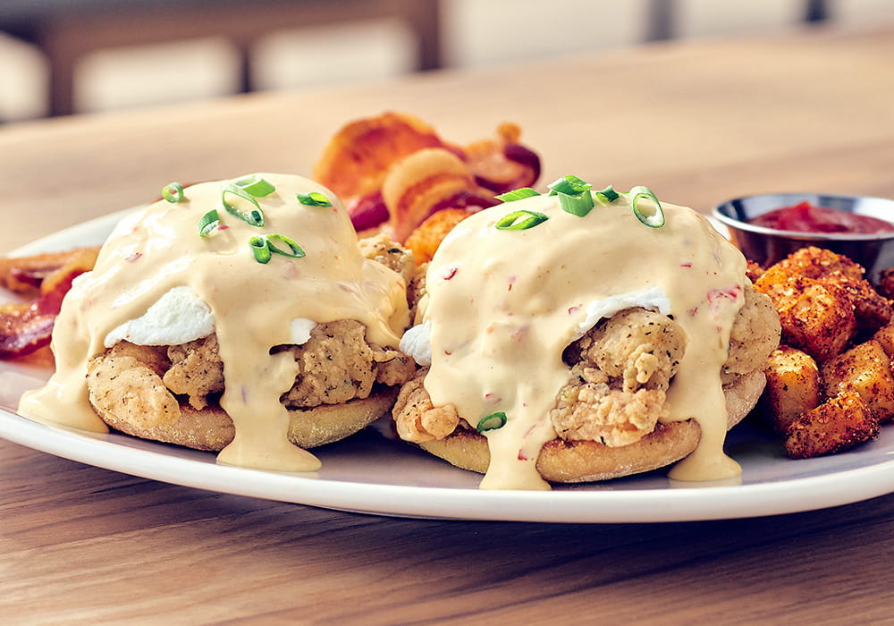 BANG BANG SHRIMP® EGGS BENEDICT Our signature crispy shrimp on a toasted English muffin, topped with poached eggs coated in creamy spicy hollandaise sauce finished with green onion, served with seasoned breakfast potatoes and applewood smoked bacon.