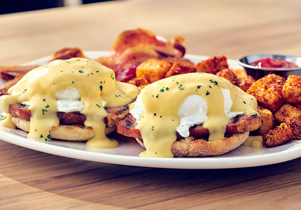 TRADITIONAL EGGS BENEDICT Smoked ham on a toasted English muffin with poached eggs and hollandaise sauce, served with seasoned breakfast potatoes and applewood smoked bacon.