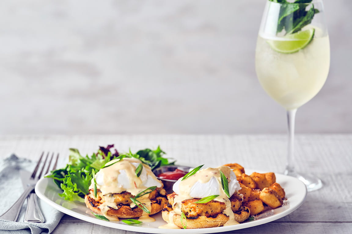 COURSE 2 CRAB CAKE BENEDICTLump crab cakes on a toasted English muffin with poached eggs and signature hollandaise sauce, served with seasoned breakfast potatoes and light citrus herb greens.  HUGO SPRITZ St~Germain elderflower liqueur and sparkling wine, with fresh mint leaves and a splash of sparkling water gives the pairing an effervescent sparkle that lifts the rich hollandaise and sweet lump crab for delicious flavor depth.