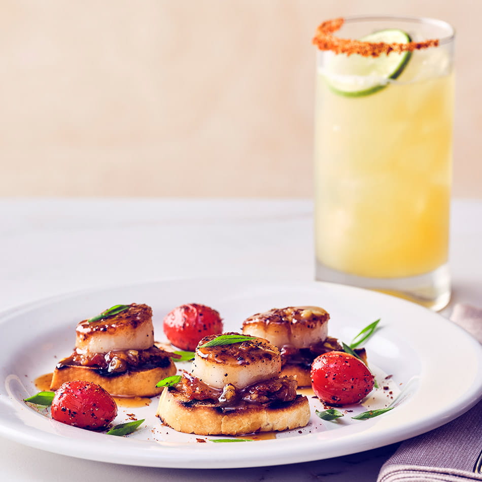 COURSE 1  SEARED SCALLOP* CROSTINI Pan-seared sea scallops finished with a bourbon glaze, served on a grilled crostini topped with bacon jam.  BOURBON MARGARITA Knob Creek bourbon and Sauza Gold tequila come together with fresh sour mix and bright orange juice, finished with a Tajín rim for a bold, smoky-citrus margarita. The subtle smokiness from the bourbon and tequila echoes the caramelized crust on the pan-seared scallops, creating a seamless flavor bridge.