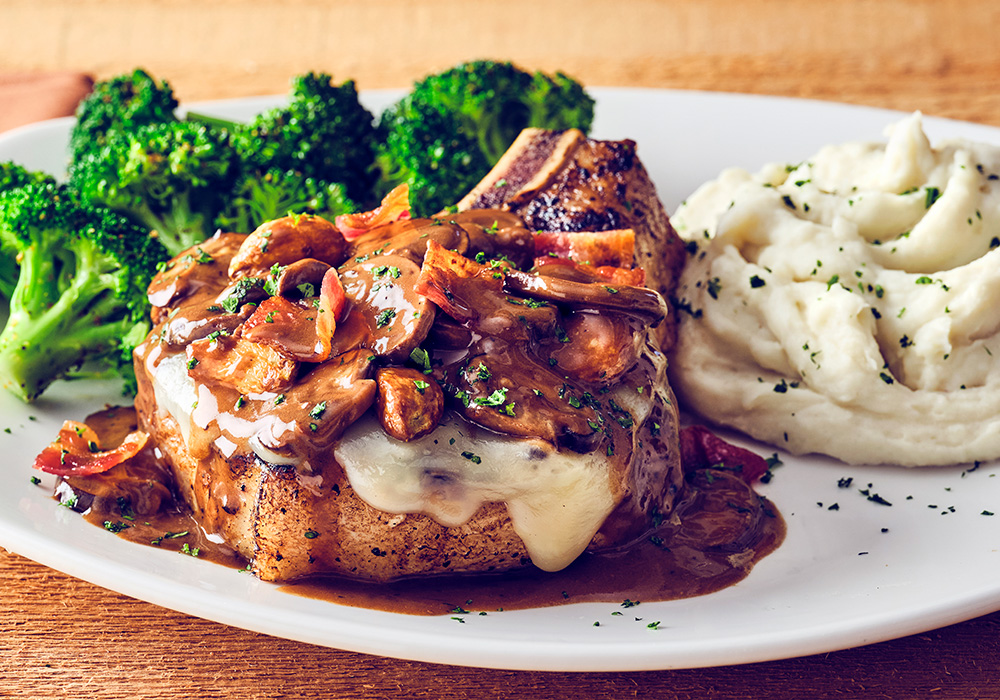 BONE-IN FONTINA PORK CHOP Wood-grilled, 12 oz, topped with fontina cheese, garlic, bacon and mushroom marsala wine sauce.