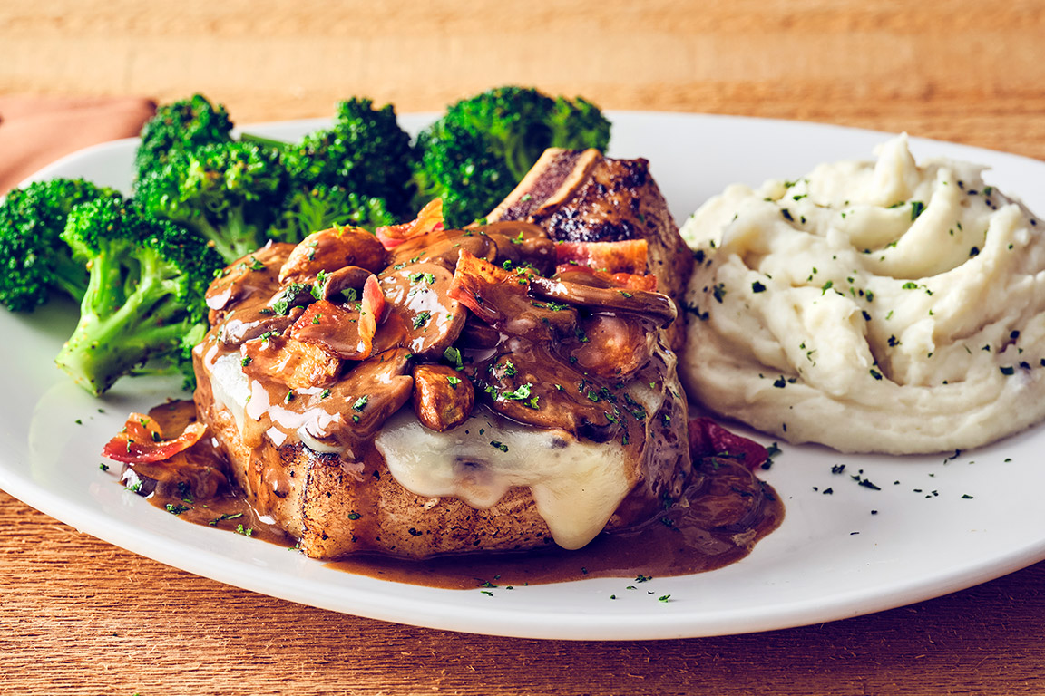 BONE-IN FONTINA PORK CHOP Wood-grilled, 12 oz, topped with fontina cheese, garlic, bacon and mushroom marsala wine sauce.