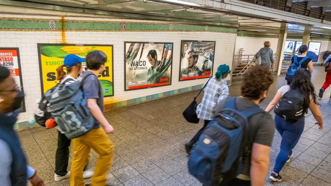 Commuters walking past two-sheet posters in a subway station