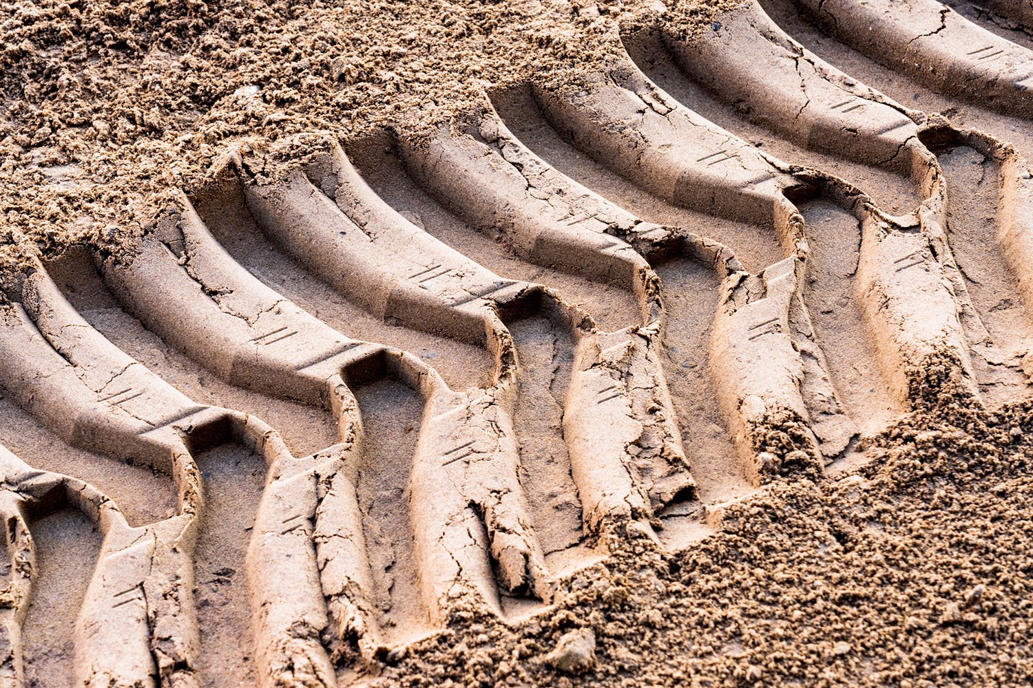Image of heavy machinery tire tracks imprinted in dirt, showcasing the robust and impactful presence of industrial machinery.