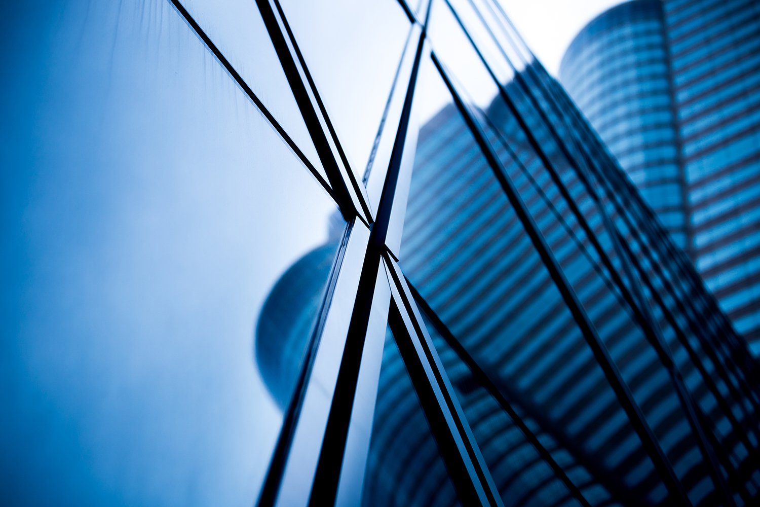 A captivating view from below a towering skyscraper, with the reflective glass facade mirroring the shapes of neighboring skyscrapers against a clear sky.