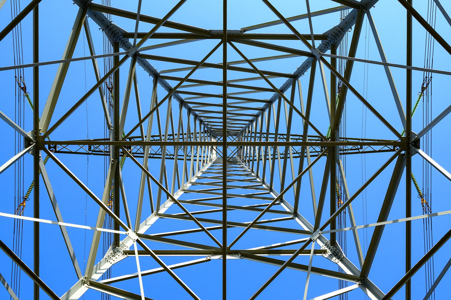 An upward view of a transmission tower from its base, showcasing its intricate steel structure set against a clear sky, embodying the power and engineering excellence of a leading multi-state utility provider.