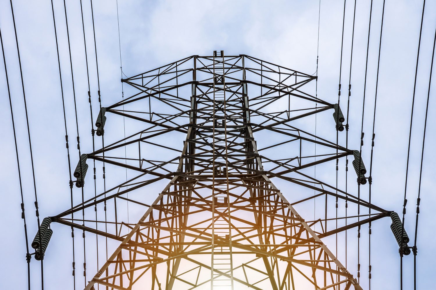 A captivating view looking up at a transmission tower against a clear blue sky, highlighting the intricate engineering and towering presence of modern utility infrastructure.