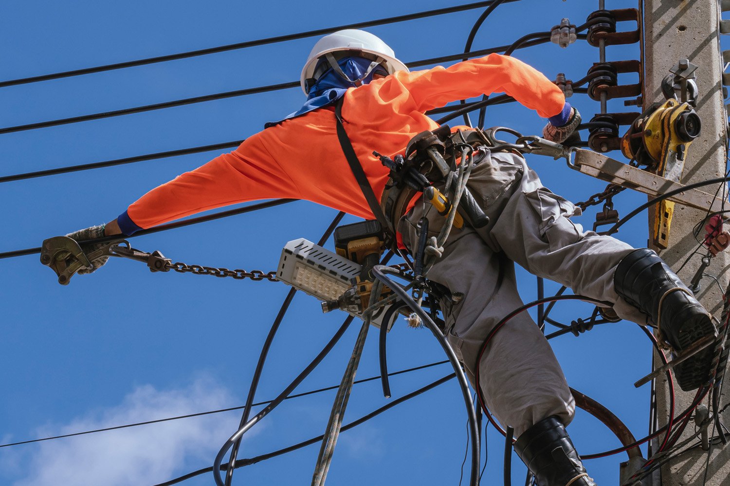 A utility worker in a hard hat and safety gear repairing power lines on a clear day