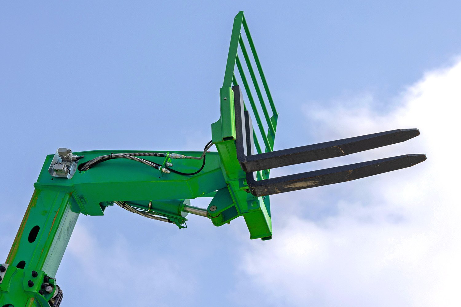A green piece of construction equipment set against a clear sky, showcasing its robust design and functionality, perfect for heavy-duty tasks.