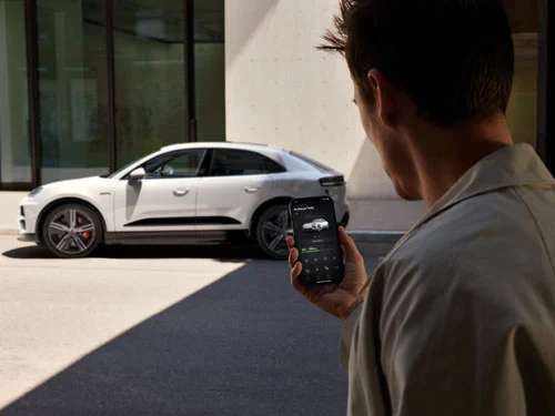 Man on Porsche connect app in front of white Porsche Macan turbo electric