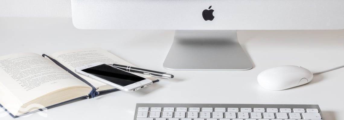 Apple imac with keyboard in front and iphone placed to the left on top of book