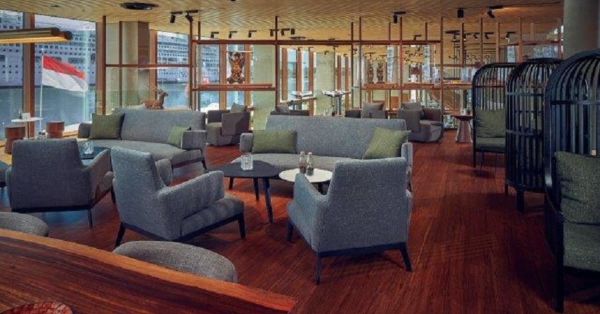 Luxe lounge van Hotel Jakarta Amsterdam met comfortabele grijze zitbanken, houten vloer en uitzicht op het water met Indonesische vlag