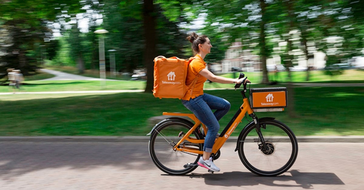 Bezorger van Thuisbezorgd.nl fietst door een park met een oranje bezorgtas en oranje fiets