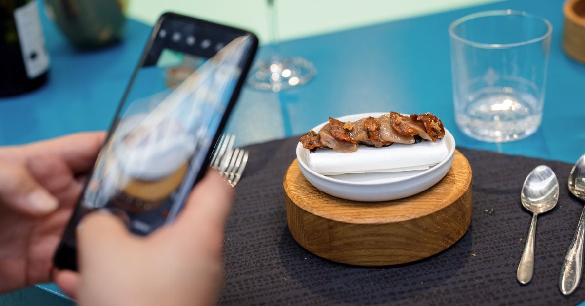 Persoon maakt foto van een culinair gerecht op een houten standaard