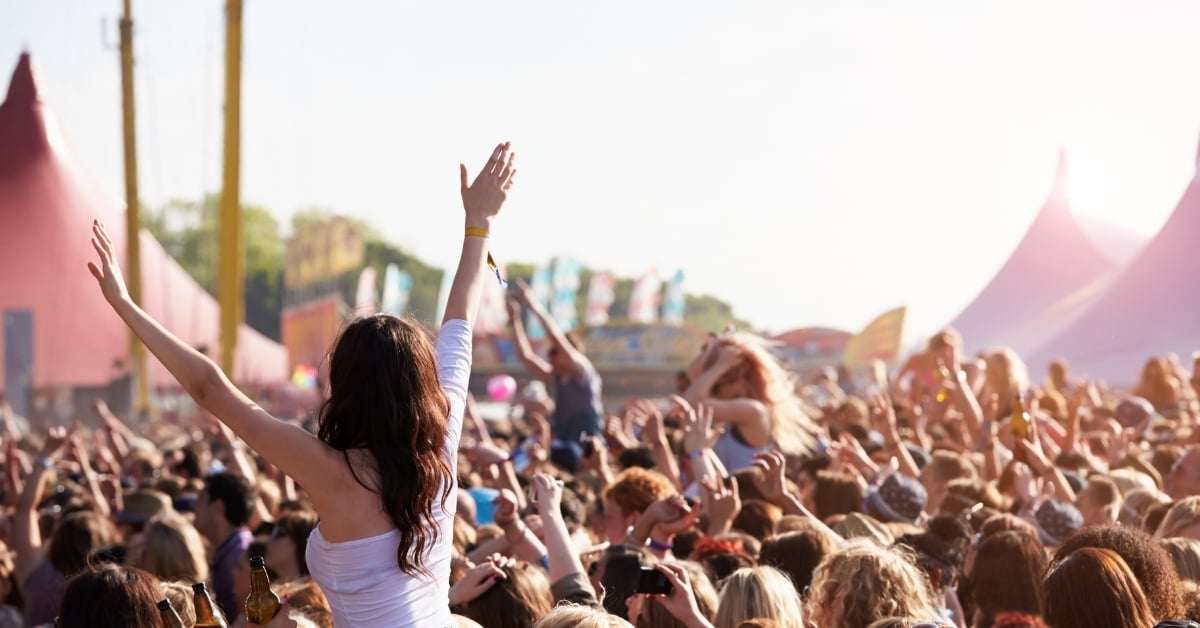Mensen dansen en feesten op een openluchtfestival, met kleurrijke tenten en vlaggen op de achtergrond
