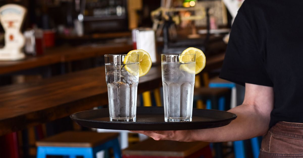 Horecamedewerker serveert twee glazen koud water met citroen op een dienblad