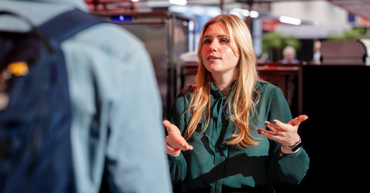 Vrouw met blond haar en groene blouse in gesprek met bezoeker tijdens horecabeurs