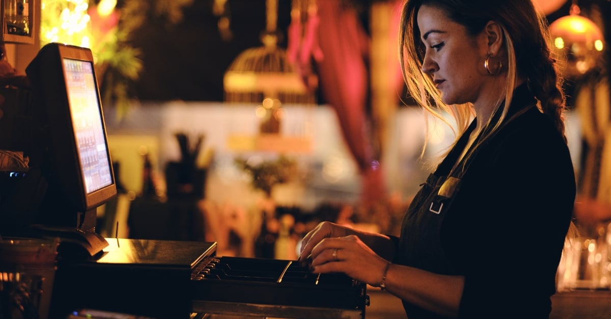 Medewerker in de horeca achter de bar bezig met de kassa in een sfeervolle werkomgeving