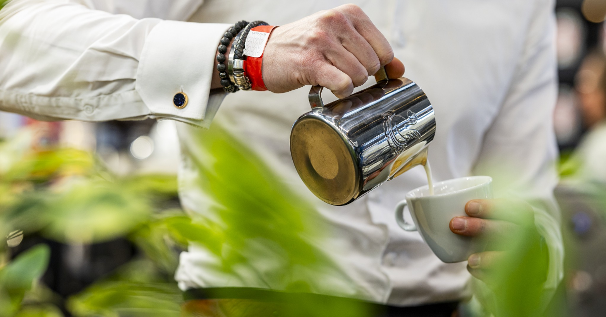 Barista schenkt opgeschuimde melk in een koffiekopje tussen de planten