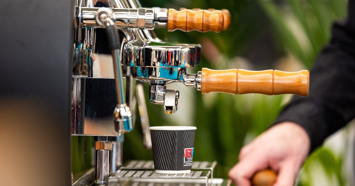 Close-up van een espressomachine met houten hendels die koffie zet in een kartonnen beker