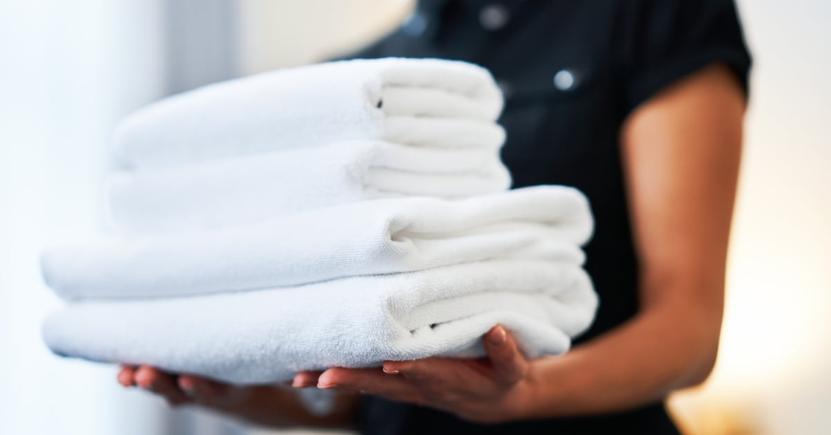 Housekeepingmedewerker met een stapel schone, witte handdoeken in een hotelkamer
