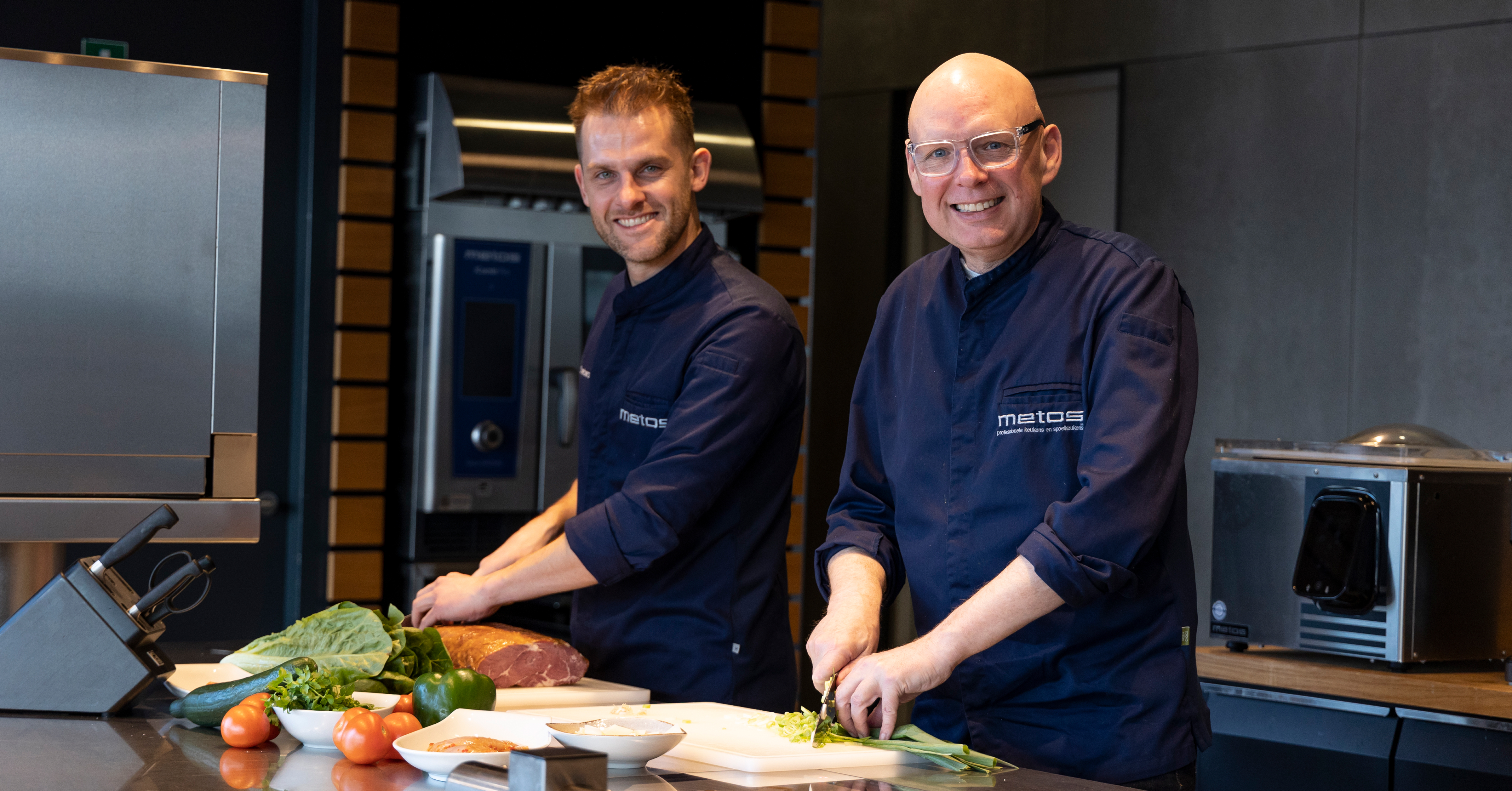 Twee chefs van Metos bereiden samen verse ingrediënten in een professionele keuken.