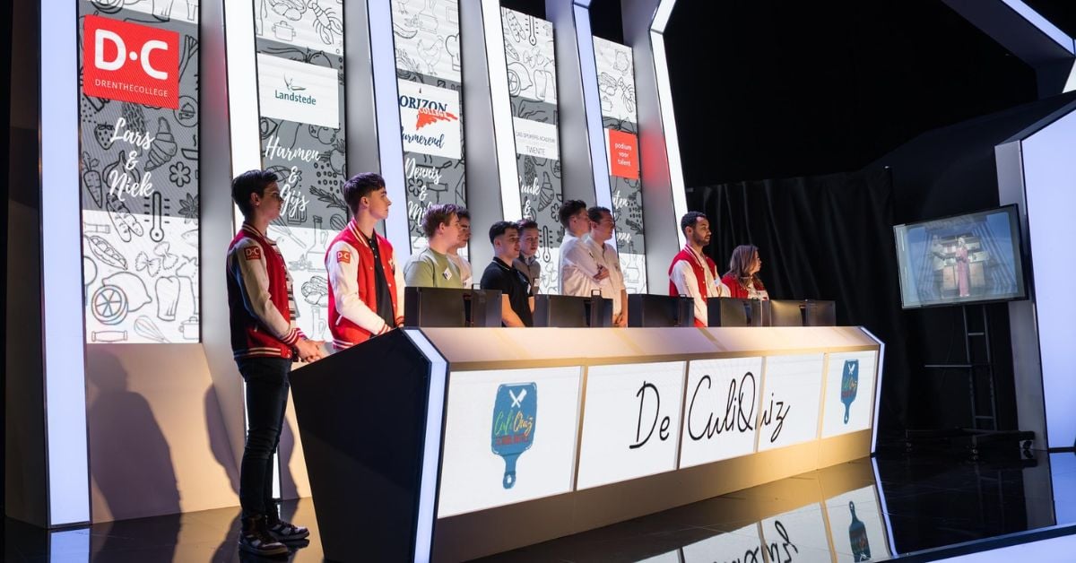 Studenten staan achter quiztafels tijdens de CuliQuiz Battle
